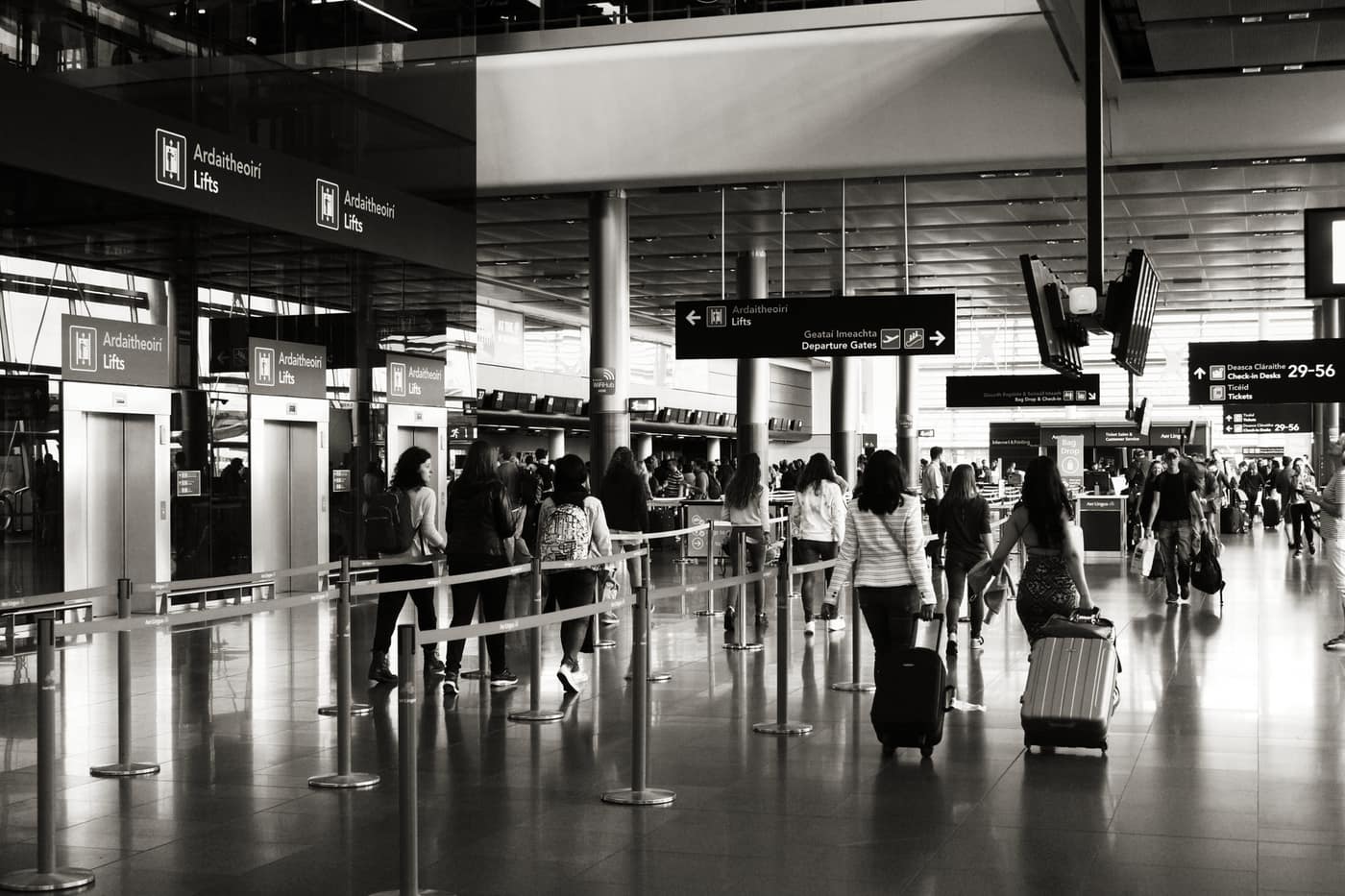 Travelers with cabin bags moving through an airport departures area