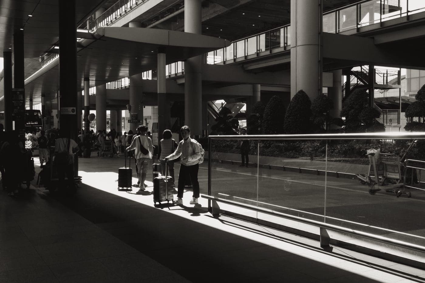 Travelers wheeling cabin cases through a sunlit airport terminal concourse