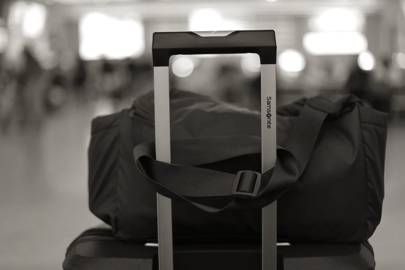 A soft duffel stacked on a wheeled suitcase in an airport terminal