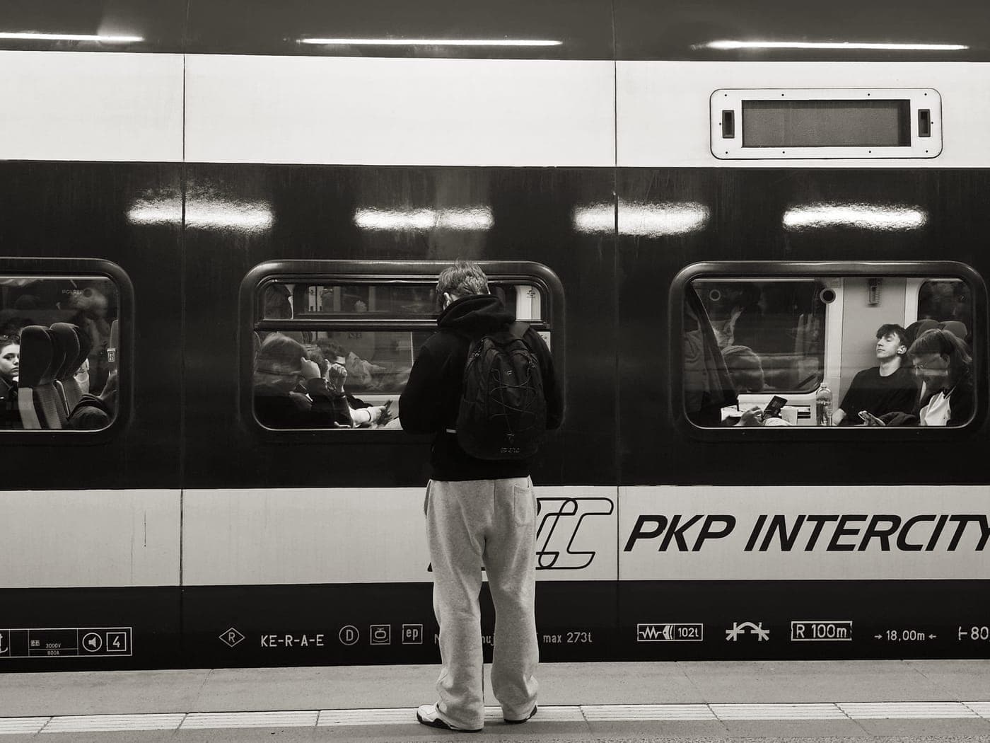 A traveler with a backpack beside another with a wheeled suitcase on a platform